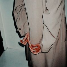 a man in a trench coat is holding his hand on the back of his jacket