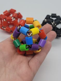 a hand holding several different colored bracelets in it's palm, with one being held by the other