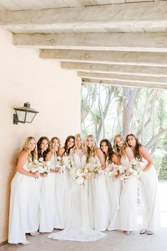 a group of women standing next to each other wearing white dresses and holding bouquets