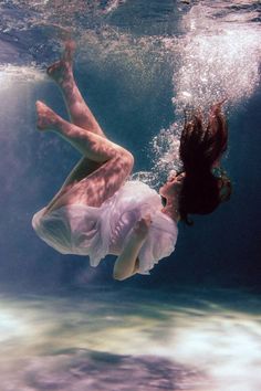 a woman floating in the water wearing a white dress