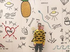 a man standing in front of a wall with drawings on it and a pineapple painted on the wall