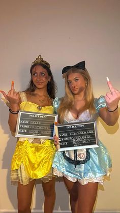 two women dressed in costumes holding up signs and giving the peace sign with their hands