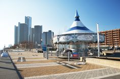 a merry go round sits on the sidewalk in front of tall buildings and skyscrapers