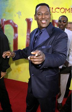 a man in a suit and tie standing on a red carpet with his hands out