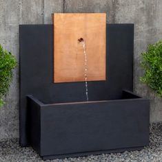 an outdoor fountain with water running from it's sides and two plants in the background