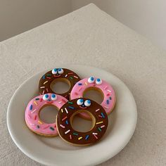 three donuts with pink frosting and sprinkles on a white plate