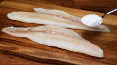 two raw fish fillets on a wooden cutting board with a spoon in one of them