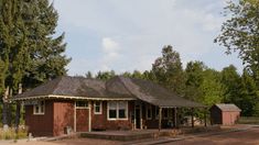 a small brown building sitting in the middle of a forest next to a train track