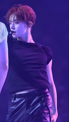 a male in a black shirt and some purple lights with his hand on his hip