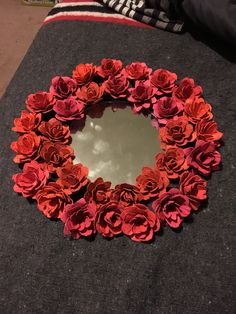 a mirror with red flowers on it sitting on a black cloth covered table next to a striped blanket