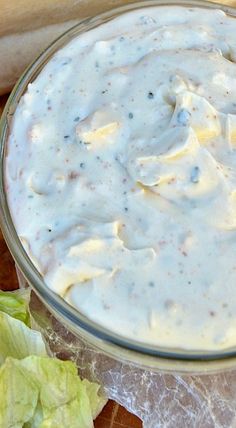 a glass bowl filled with white sauce next to lettuce