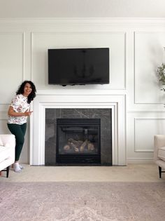 a woman standing in front of a fireplace with a tv on it's wall