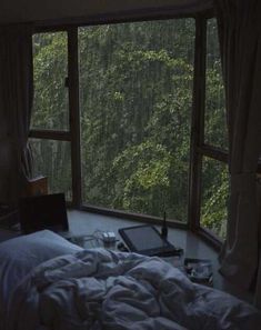 a laptop computer sitting on top of a bed in front of a window next to a forest