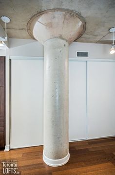 a large white column in the middle of a room with wooden floors and ceiling lights