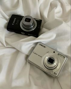 a digital camera sitting on top of a white bed sheet next to it's case