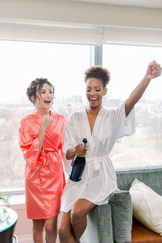 two women in robes are sitting on a couch and one is raising her arm up