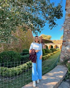 a woman standing on steps in front of a stone building with trees and bushes behind her