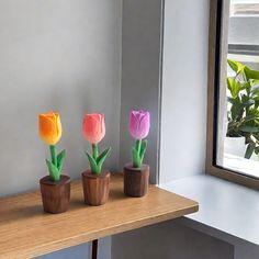 three wooden vases with flowers in them sitting on a table next to a window