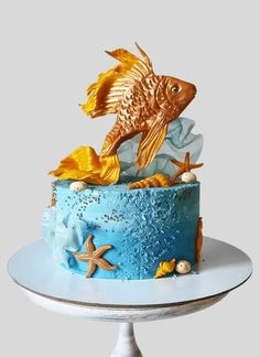 a blue cake with gold fish and starfish on top, sitting on a white pedestal