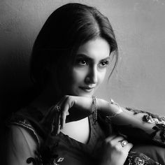 a black and white photo of a woman with jewelry on her arm, leaning against a wall