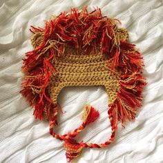 a crocheted hat with red fringes on top of a white bed sheet