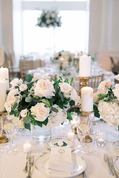 the table is set with white flowers, candles and place settings for an elegant dinner