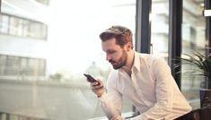 a man looking at his cell phone while sitting in an office building window sill