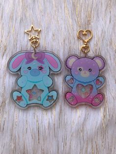 two key chains that are shaped like teddy bears with hearts on them, one is pink and the other is blue