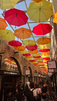 many colorful umbrellas are hanging from the ceiling in this shopping area, while people walk underneath them