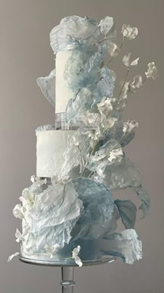 a three - tiered cake with white flowers and blue icing on a silver stand