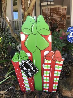 a green and red wooden sign with presents on it's front lawn in front of a house