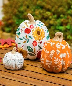 three painted pumpkins sitting on top of a wooden table