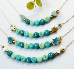 three necklaces with name and star charms hanging from them on a white table next to a potted plant