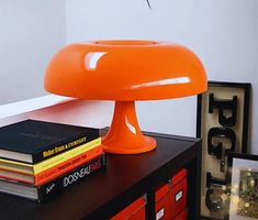 an orange lamp sitting on top of a table next to some books and a framed photograph