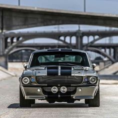 an old muscle car parked in front of a bridge