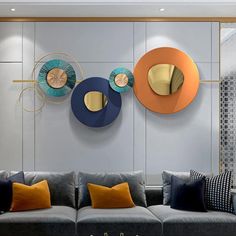 three circular mirrors on the wall above a gray couch in a living room with orange and blue pillows