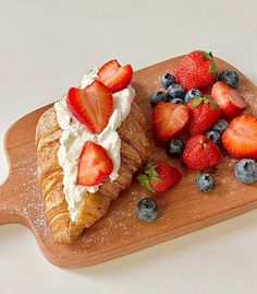 a pastry with whipped cream, strawberries and blueberries on it sitting on a cutting board