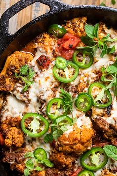 a skillet filled with meat, cheese and green peppers on top of a wooden table