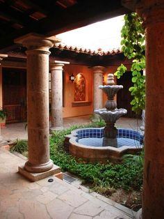 an outdoor fountain in the middle of a courtyard with columns and plants on either side