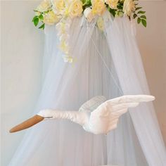 a white bird is hanging from a string with flowers in the background and a canopy behind it