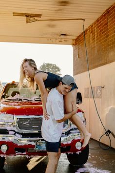 a man and woman standing on the hood of a red pickup truck with their arms around each other