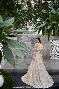 a woman in a long dress is standing near some trees and plants with her back to the camera