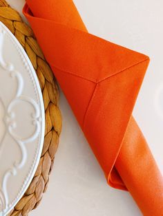 an orange napkin on top of a white plate next to a basket with an orange ribbon