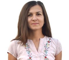 a woman with long brown hair wearing a pink shirt and blue jeans is looking at the camera