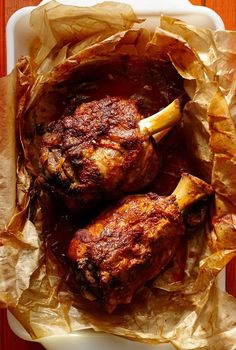 two cooked meats in a white dish with brown paper on the side and a wooden table