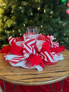 a wine glass is sitting on a table with red and white ribbons around it, in front of a christmas tree