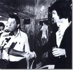 black and white photograph of two men shaking hands with microphones in front of them