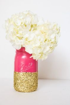 a pink mason jar filled with white hydrangeas and gold glitter accents, sitting on a table