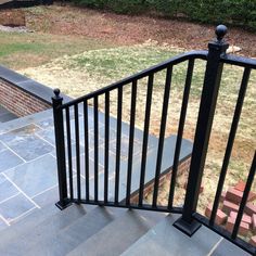 an iron railing on the side of a brick building with grass and bushes in the background