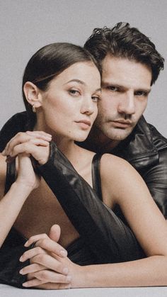 a man and woman are posing for a photo in front of a gray background with their arms around each other